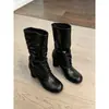 Nova coleção 2026: Botas femininas de cano médio com tiras e saltos grossos, perfeitas para outono e inverno, apresentando um design emagrecedor com detalhes plissados e um visual de salto alto estilo equestre.