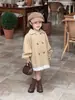 Chegada Nova Outono 2026 Estilo Coreano Roupas Infantis Casaco Trench Coat Feminino de Comprimento Médio com Acabamento em Renda e Laço nas Costas em Estilo Britânico