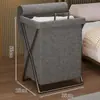 Uma cesta de lavanderia prática para colocar roupas perto da cama no quarto à noite; uma cesta de lavanderia dobrável para roupas sujas; uma cesta de lavanderia doméstica para guardar roupas sujas