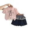 Nuevo atuendo de verano 2026 para niñas: conjunto elegante de manga corta con cuello, que presenta una camisa de dibujos animados y una falda corta, disponible para venta al por mayor