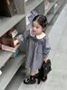 Roupas infantis coreanas, nova coleção outono 2026: vestido xadrez com gola boneca para bebês meninas, apresentando um estilo pastoral e fresco, adequado para exportação