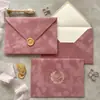 Sobre de terciopelo marrón oscuro con logo de marca estampado en dorado, tarjeta acrílica de borde dorado irregular, invitación de negocios