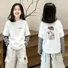 Camiseta Manga Longa Infantil 2026 Primavera/Outono Nova Estampa Cartoon para Crianças de Tamanho Médio a Grande Algodão Puro Listrada Falsa Peça Dupla Camisa Base