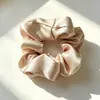 La scrunchie de satén tiene una textura suave y brillante, está disponible en múltiples colores, tiene un tacto lujoso, ofrece elasticidad moderada y sujeta el cabello de forma segura.