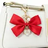 Suministros del fabricante lazo de tela de algodón poliéster etiqueta con forma de corazón de aleación charm de bolso de mano con perla sintética llavero para equipaje de mujer