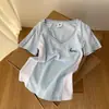 Camiseta Retrô Americana com Costura em Cor Contrastante Decote V Ombro Direito Manga Curta para Mulheres Design de Verão Efeito Emagrecedor Top Curto Tendência