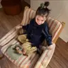 La nueva colección de otoño 2026 para niñas estilo bosque incluye una sencilla camisa de cuadros con cuello, un chaleco de punto con botones de cuerno y pantalones de pierna recta.