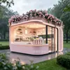 Tienda de postres tipo cápsula espacial rosa con esquinas redondeadas, decorada con plantas florales y verdes en la parte superior, una cafetería y tienda de bebidas popular en una zona montañosa escénica