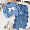 Estilo europeo y americano: un atuendo de niña dulce y delicado que presenta un top blanco, suave y de manga larga con un diseño de lazo completo en el lateral, combinado con pantalones de mezclilla - un conjunto de dos piezas