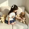 Novo Modelo de Comércio Exterior 2026 Estilo Coreano Verão Novo Conjunto de Duas Peças para Meninas com Estampa de Urso, Top de Manga Curta Dividido e Saia Plissada Xadrez