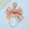 Correa para teléfono con lazo de color sólido estilo francés y perla, llavero con colgante de insignia redonda, accesorio versátil para bolso para niñas