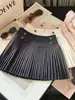 Falda corta de lana estilo coreano con hebilla dorada para mujer 2026 Otoño/Invierno Nueva falda plisada de línea A versátil de cintura alta adelgazante anti-exposición