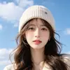 Gorro de punto de color liso de moda versátil para invierno con decoración de logotipo metálico, gorro cálido a prueba de viento para protección de orejas al aire libre