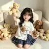 Novo Modelo de Comércio Exterior 2026 Estilo Coreano Verão Novo Conjunto de Duas Peças para Meninas com Estampa de Urso, Top de Manga Curta Dividido e Saia Plissada Xadrez