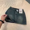 Mini saia jeans de cintura alta estilo retrô de Hong Kong para mulheres, novo modelo 2026, anti-exposição, corte A, justa ao quadril, emagrecedora, versátil, moderna, cor sólida
