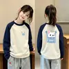 Camiseta infantil moderna e estilosa com blocos de cor, gola redonda, mangas compridas e estampa de desenho animado, perfeita como camada base para o outono e inverno de 2026