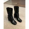 Nova coleção 2026: Botas femininas de cano médio com tiras e saltos grossos, perfeitas para outono e inverno, apresentando um design emagrecedor com detalhes plissados e um visual de salto alto estilo equestre.