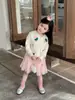 Coleção Outono 2026: Roupas infantis estilo coreano, apresentando um cardigã de tricô com desenho animado e uma saia fofa de tule com pompons para meninas