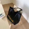 Bolsa tote simples e descontraída em azul claro com letras para estudantes universitárias, adequada para o trajeto matinal, passeios e piqueniques.