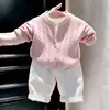 Ropa infantil coreana 2026 colección otoño/invierno nueva: conjunto de suéter rosa de punto trenzado, cárdigan de punto y pantalones casuales blancos para niños y niñas