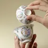 En las montañas, pinos y mariposas danzan entre las flores.; un cuenco de té de cerámica pintado de rosa, hecho a mano con un cuerpo delgado que no quema la mano, es parte del juego de té Kung Fu
