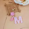 Llavero de letra inglesa rosa, un accesorio lindo y moderno con un pompón esponjoso y un borla, perfecto para proyectos de bricolaje y como charm para bolso para mujeres