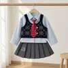 Conjunto de três peças outonal para bebês meninas: uma camisa de manga longa com gola em estilo preppy, combinada com um colete de padrão losango e uma saia plissada com cós elástico.