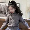 Ropa infantil estilo coreano 2026 colección otoño e invierno nueva: cárdigan de punto gris dulce con lazo para niña y falda de cuadros azules, moderno