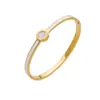 Este elegante brazalete esmaltado en oro y azul presenta un diseño elegante con un delicado centro esmaltado en blanco, lo que lo convierte en el accesorio perfecto tanto para ocasiones casuales como formales. El diseño atemporal añade un toque refinado a tu guardarropa.