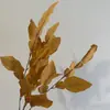 Arrume arranjos florais com cachos de folhas de toranja para realçar a altura do teto em um salão de casamento com tema de floresta, e use folhas decorativas para montar uma parede de fundo.