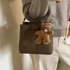 Bolso de hombro estilo coreano para el otoño de 2026, con un pequeño charm de oso, un bolso tipo cubo nuevo y elegante para mujer, simple y versátil