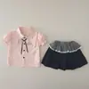 Nuevo atuendo de verano 2026 para niñas: conjunto elegante de manga corta con cuello, que presenta una camisa de dibujos animados y una falda corta, disponible para venta al por mayor