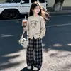 Roupa de outono para meninas: um conjunto de duas peças composto por uma calça xadrez de perna larga e um suéter de tricô com estampa de ursinho, em um novo estilo coreano de 2025, perfeito para uso casual