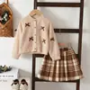Nuevo producto de otoño transfronterizo para niñas: Conjunto otoñal de estilo europeo y americano con lazo, cárdigan de manga larga, minifalda de cuadros y conjunto de dos piezas Maillard