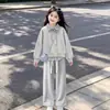 Atuendo elegante y moderno para niñas 2026: top de moda tipo dos piezas con un cuello elegante, combinado con pantalones sencillos y casuales, un conjunto de dos piezas versátil