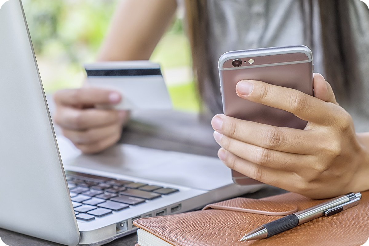 Pessoa segurando cartão de crédito e smartphone em frente a laptop, representando as formas de pagamento seguras na importação da China como T/T, escrow e carta de crédito