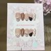 Un par de uñas postizas hechas a mano estilo francés de color rosa y crema, con diseño de lunares, forma de corazón, moño y ribete de encaje