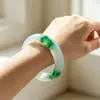 Pulsera de jade de alta calidad con una textura clara y helada y vibrantes patrones florales verdes. El jade es excepcionalmente claro y el diseño floral es vívido, realzando la elegancia de quien lo lleva.. Venta al por mayor de exquisitos brazaletes de jade para mujer
