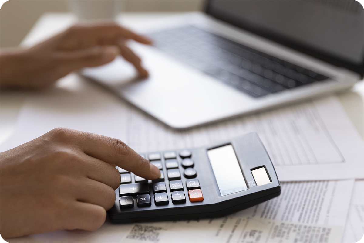 Pessoa utilizando calculadora sobre documentos fiscais ao lado de laptop, simulando o cálculo do custo total de importação da China