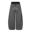 Calça trendy estilo americano de corte solto com perna curva para homens, apresentando design de retalhos, cós contrastante, bordado de letras e uma silhueta longa e fluida