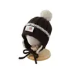 Bonito gorro de lana con logo cuadrado de osito para bebé al por mayor, elegante estilo coreano para niños, con protección para las orejas, gorro de punto forrado para otoño e invierno
