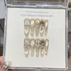 Un Diseño de Uñas Cat-Eye con Gris Champaña, Isla Dorada de los Sueños, Estilo Mil Dorados, Sonrisa Captadora de Luz, Explosión Estelar Pintada a Mano y Pedrería Apilada