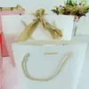 Saco de presente de papel Yuanbao Saco de presente com fita Saco de compras para roupas com placa de luz Saco de presente com corda de três fios logo impresso