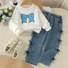 Estilo europeo y americano: un atuendo de niña dulce y delicado que presenta un top blanco, suave y de manga larga con un diseño de lazo completo en el lateral, combinado con pantalones de mezclilla - un conjunto de dos piezas