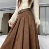 Foto real de falda midi plisada estilo coreano de otoño/invierno 2026, de ante, línea A, con dobladillo ancho, efecto de cubrir la cadera y adelgazante, viene con cinturón