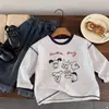 Camiseta de algodón puro para niños, modelo primavera y otoño 2026 para bebés y niños pequeños, top de dibujos animados graffiti estilo ins, camiseta interior de manga larga para niños