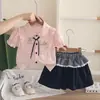 Nuevo atuendo de verano 2026 para niñas: conjunto elegante de manga corta con cuello, que presenta una camisa de dibujos animados y una falda corta, disponible para venta al por mayor