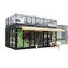 Cafetería tipo contenedor de estilo industrial con muros cortina de cristal de suelo a techo y una plataforma de observación en el nivel superior, ubicada en un distrito cultural y comercial