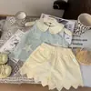 Ropa Infantil Estilo Coreano 2026 Nuevo Verano Conjunto de Dos Piezas para Niñas: Top a Cuadros con Cuello de Muñeca y Shorts con Dobladillo Ondulado