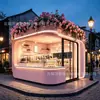 Tienda de postres tipo cápsula espacial rosa con esquinas redondeadas, decorada con plantas florales y verdes en la parte superior, una cafetería y tienda de bebidas popular en una zona montañosa escénica